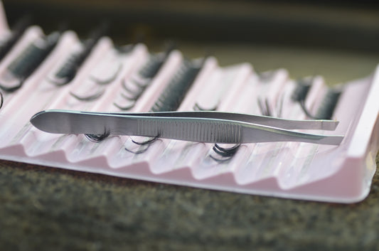 Tweezers resting on a tray of false eyelashes